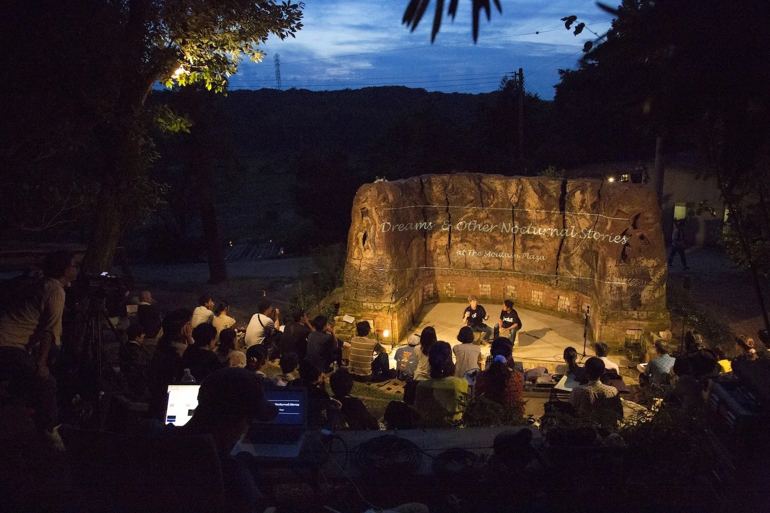 Audience gathered at The Mountain Plaza ceramic amphitheater at dusk for an outdoor performance and projection in Mihama, Aichi.／愛知県美浜町の山の広場®焼物野外劇場で、夕暮れの野外公演と映像投影を楽しむ人々。