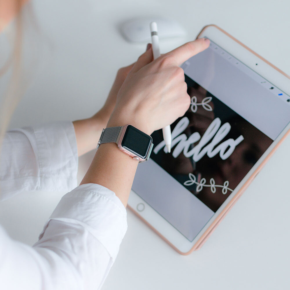 A person drawing the word 'hello' on a tablet with a stylus, wearing a smartwatch.