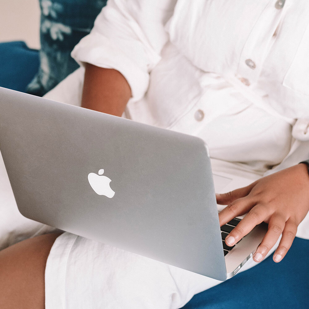 Person wearing a white shirt with rolled-up sleeves using a silver MacBook laptop.