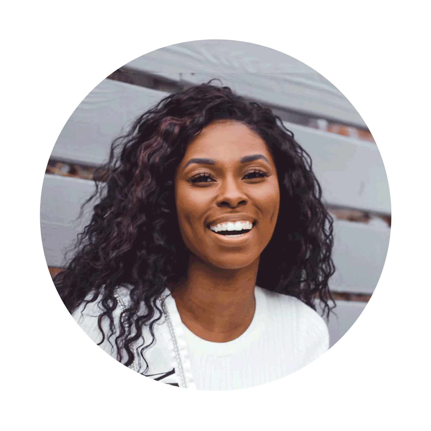 A smiling woman with curly dark hair, wearing a white top, sitting on outdoor bleachers.
