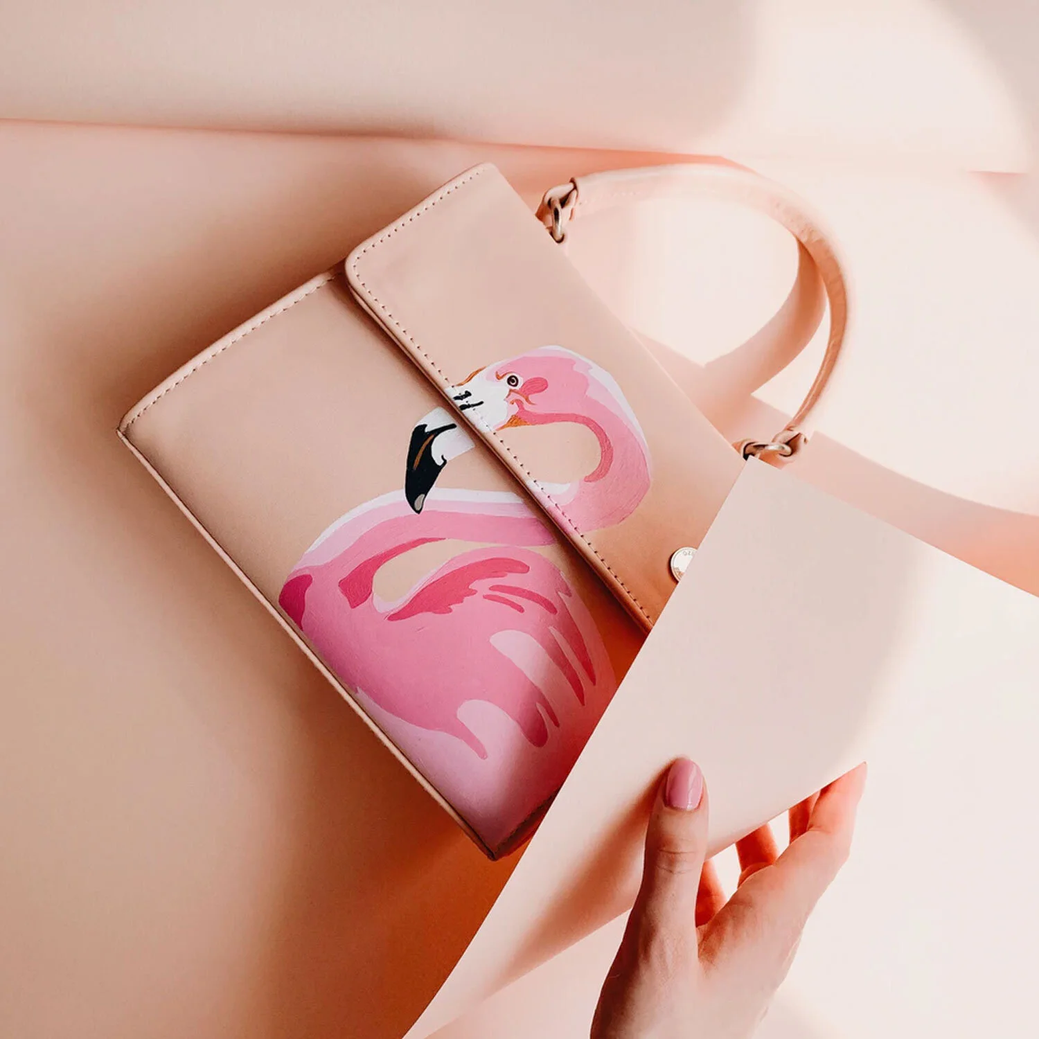 A pink handbag with a flamingo print being held over a beige background.