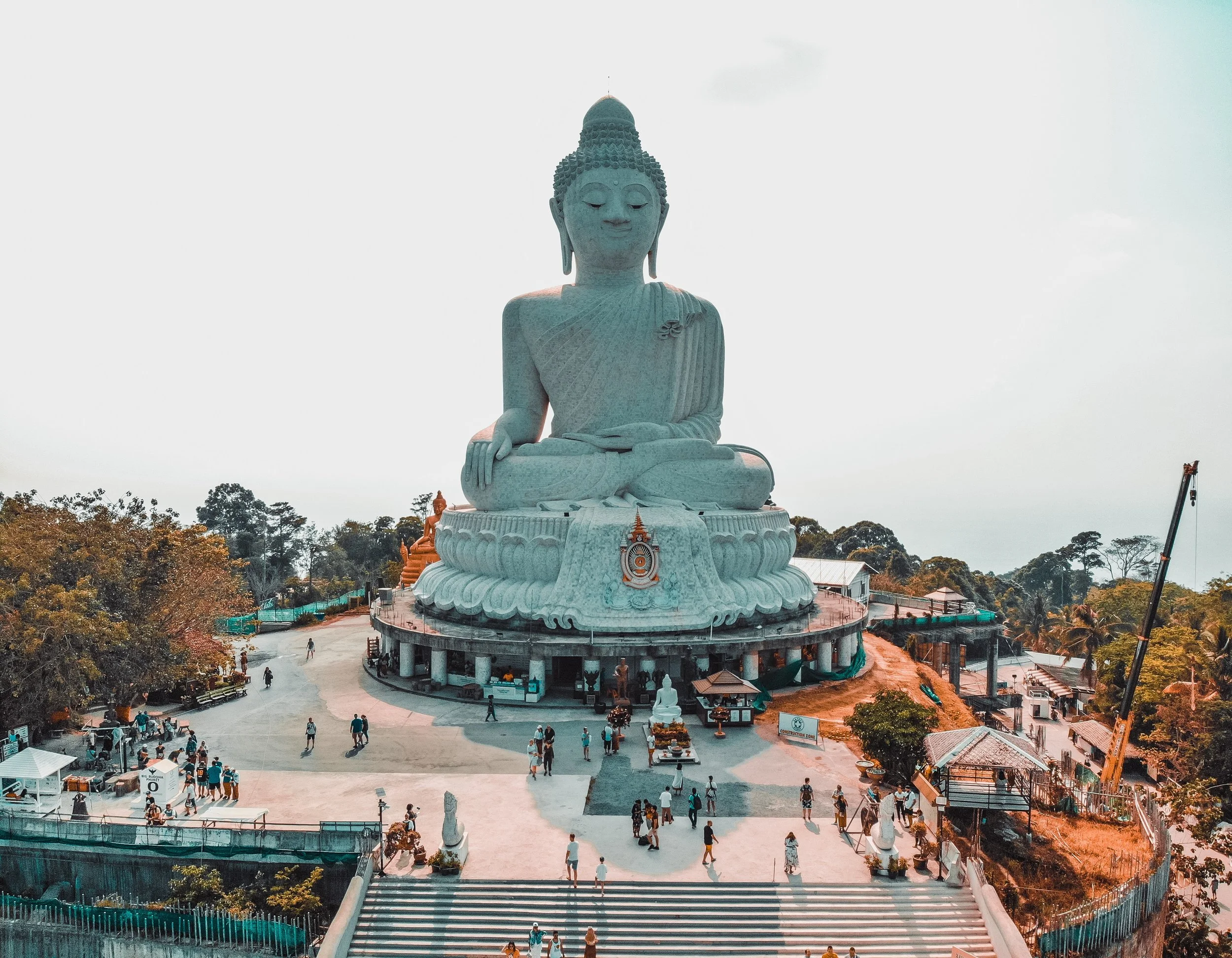 Large white Buddha statue seated on a lotus flower pedestal with people walking around it.