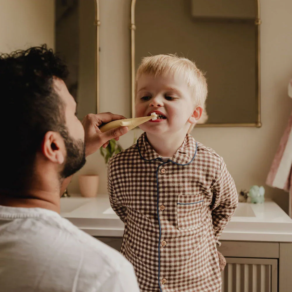 Parent helping toddler brush teeth at home, children’s oral care routine with soft toothbrush in bathroom setting