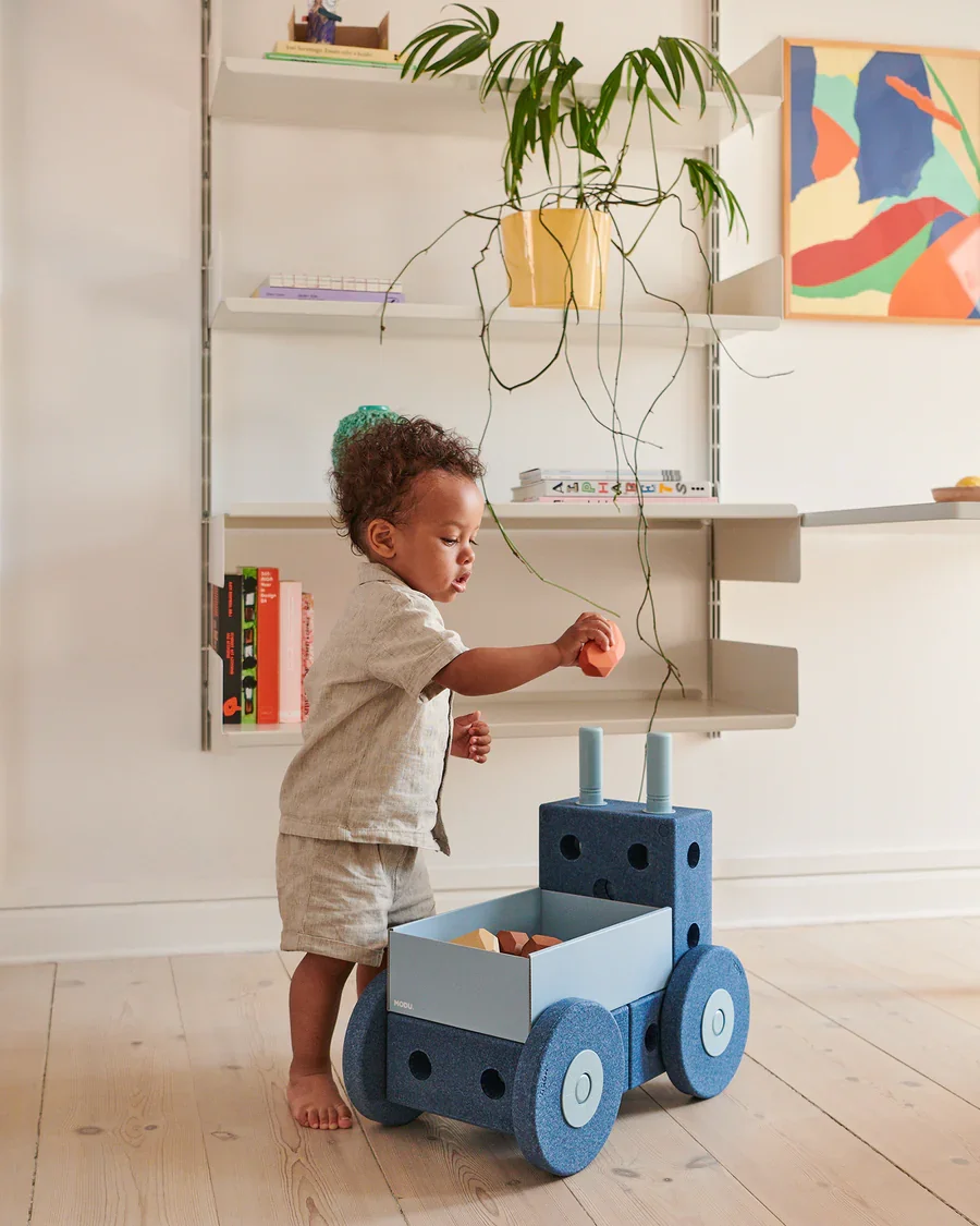 Toddler playing with MODU foam building blocks toy, stacking pieces on a wheeled cart in a bright home setting