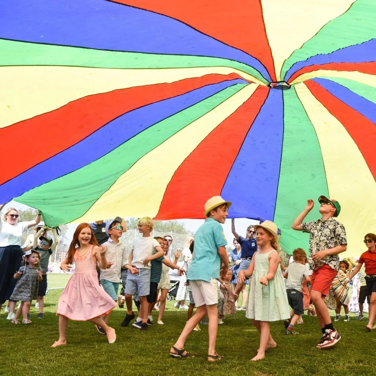 Children playing under a colourful parachute during family activities at Chestertons Polo in the Park in London.