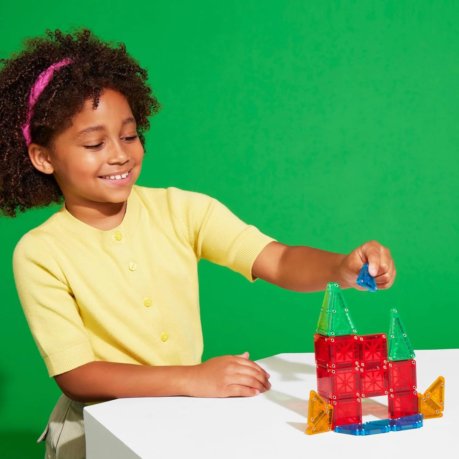 Child building a colourful castle with translucent magnetic building tiles in red green blue and orange, STEM construction toy for creative play