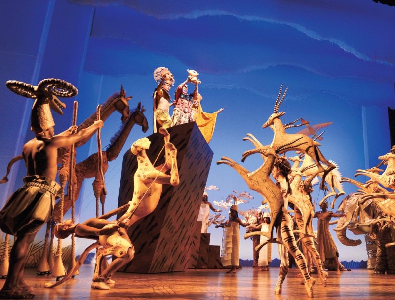 Performers on stage during The Lion King musical in London's West End with colourful costumes and African-inspired set design.