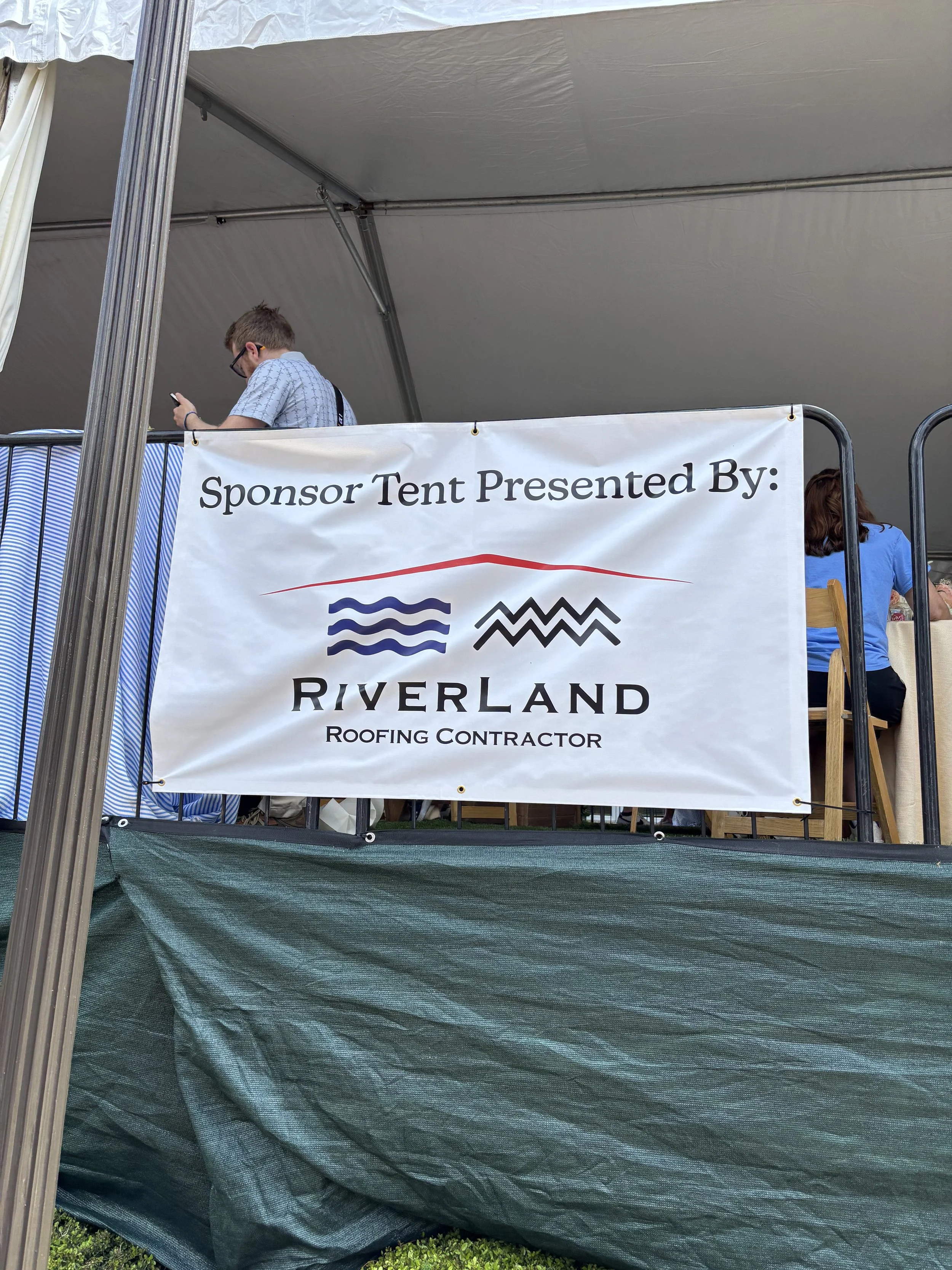 A white banner that says "Sponsor tent presented by riveralnd roofing" with the riverland logo