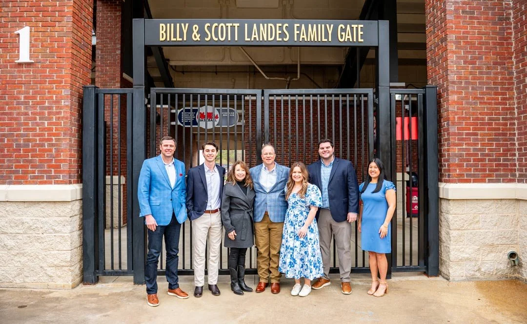 A group of people standing in front of top the Billy and Scott Landes Family Gate at the ole miss baseball stadium