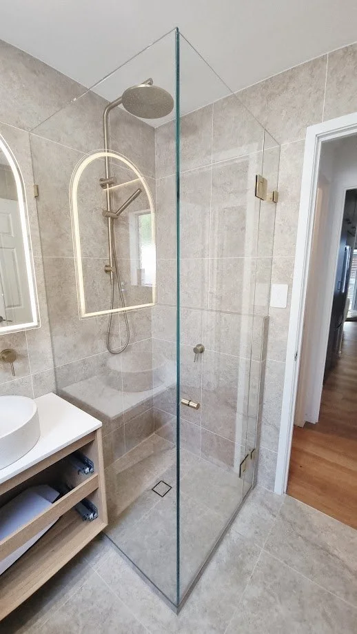 A modern walk-in shower with a glass enclosure, rain shower head, and a wall-mounted shower fixture in a tiled bathroom.