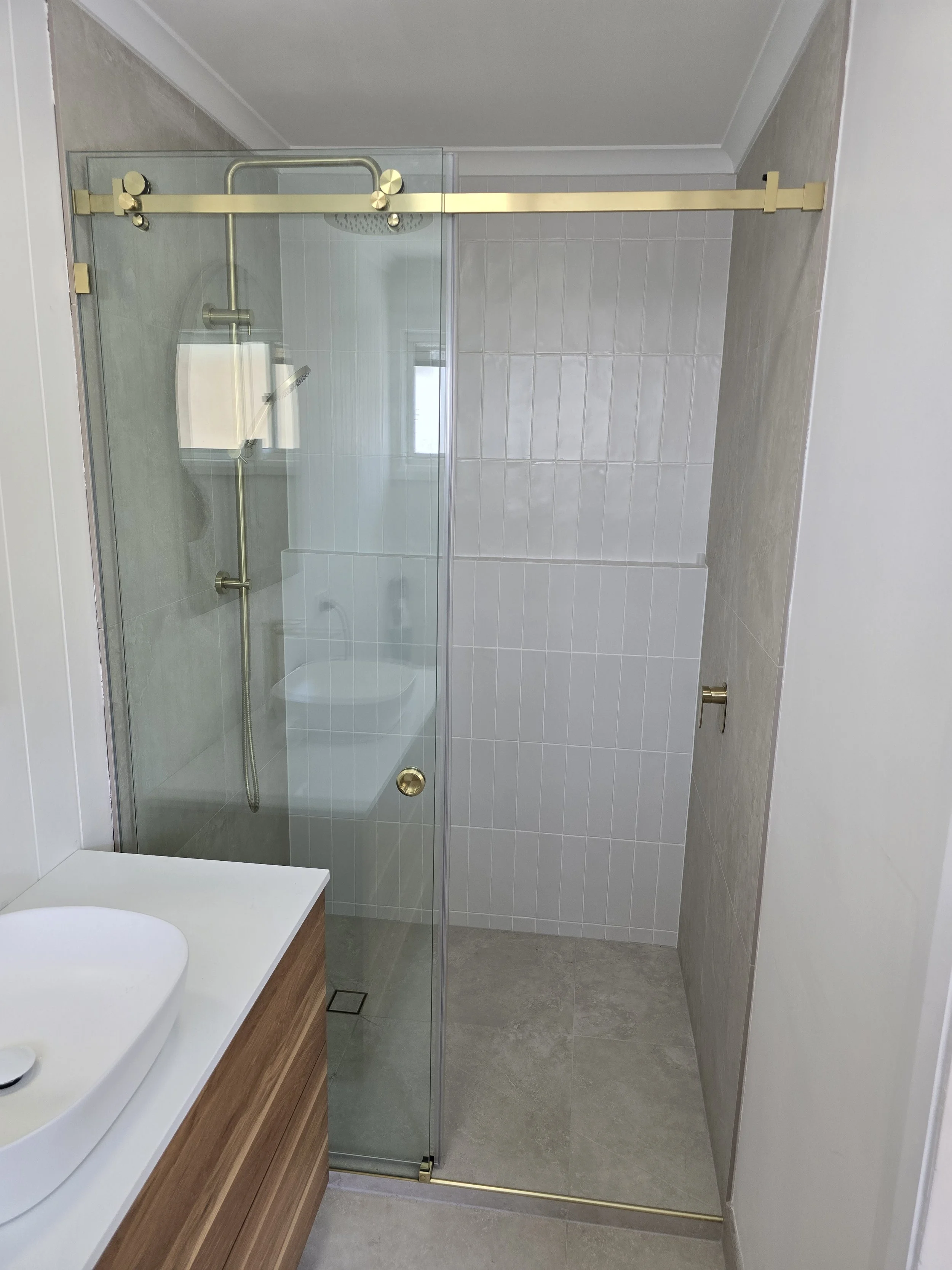 Modern bathroom with a glass shower enclosure, shower head, and a wooden vanity with a white sink.