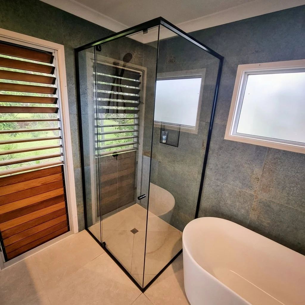 Modern bathroom with a walk-in glass shower with a matte black frame and a white countertop sink.