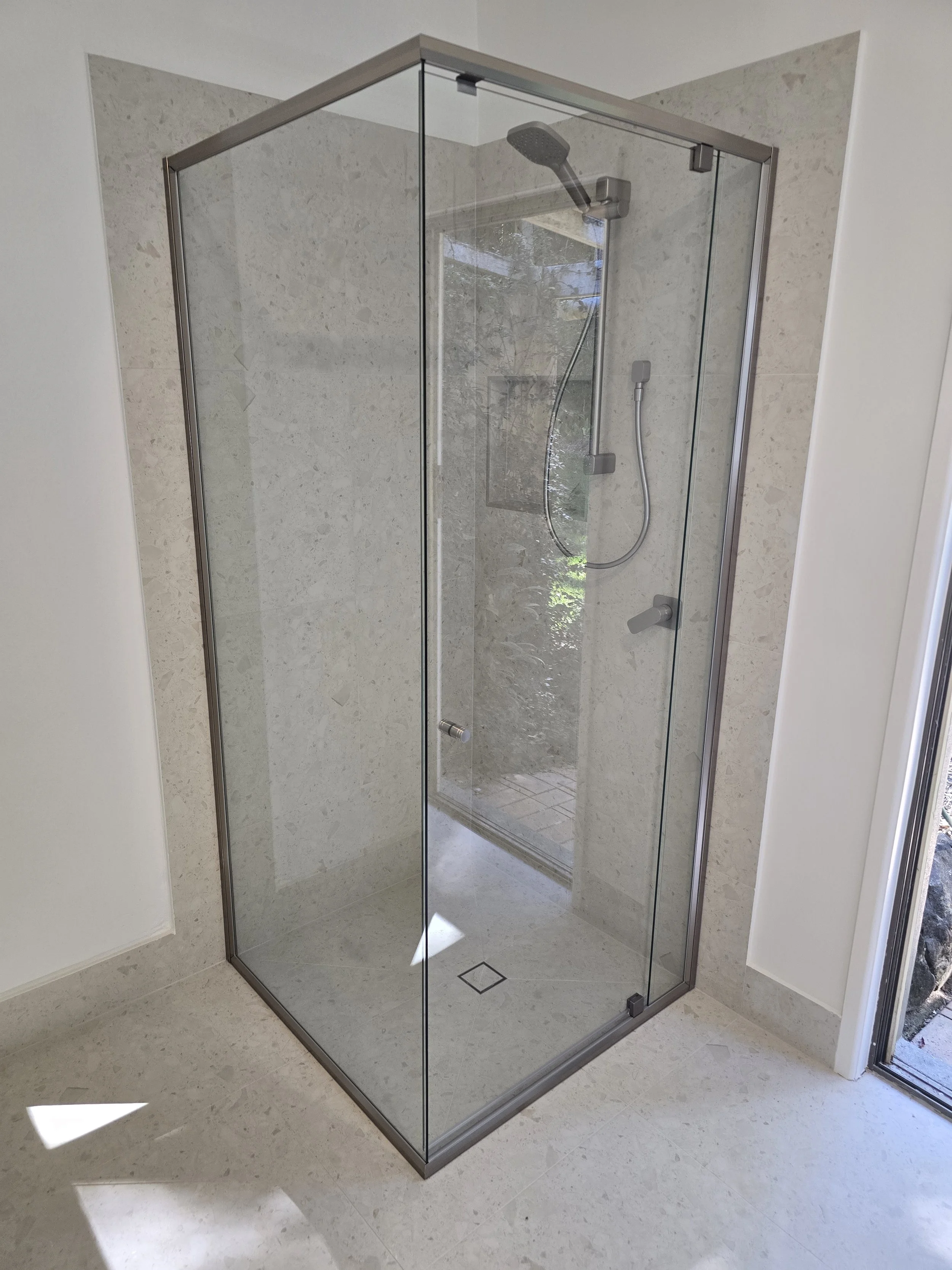 A modern glass shower enclosure with a chrome frame and a sliding door, located in a bathroom with tan tile walls and floor.