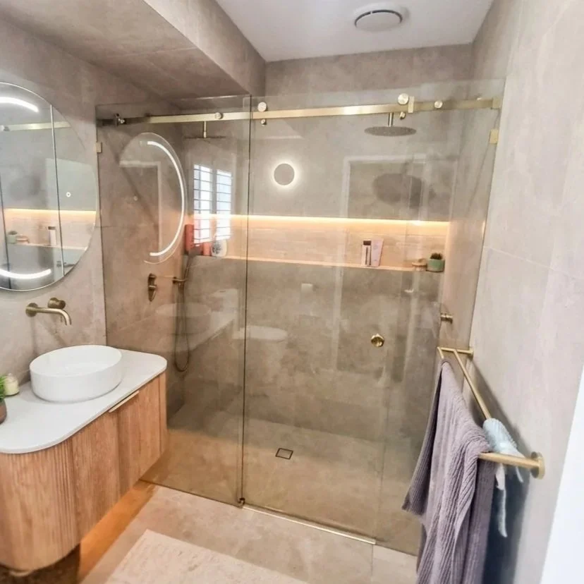 A modern glass shower with a black metal frame, black shower head, and wood-like tile flooring in a bathroom.