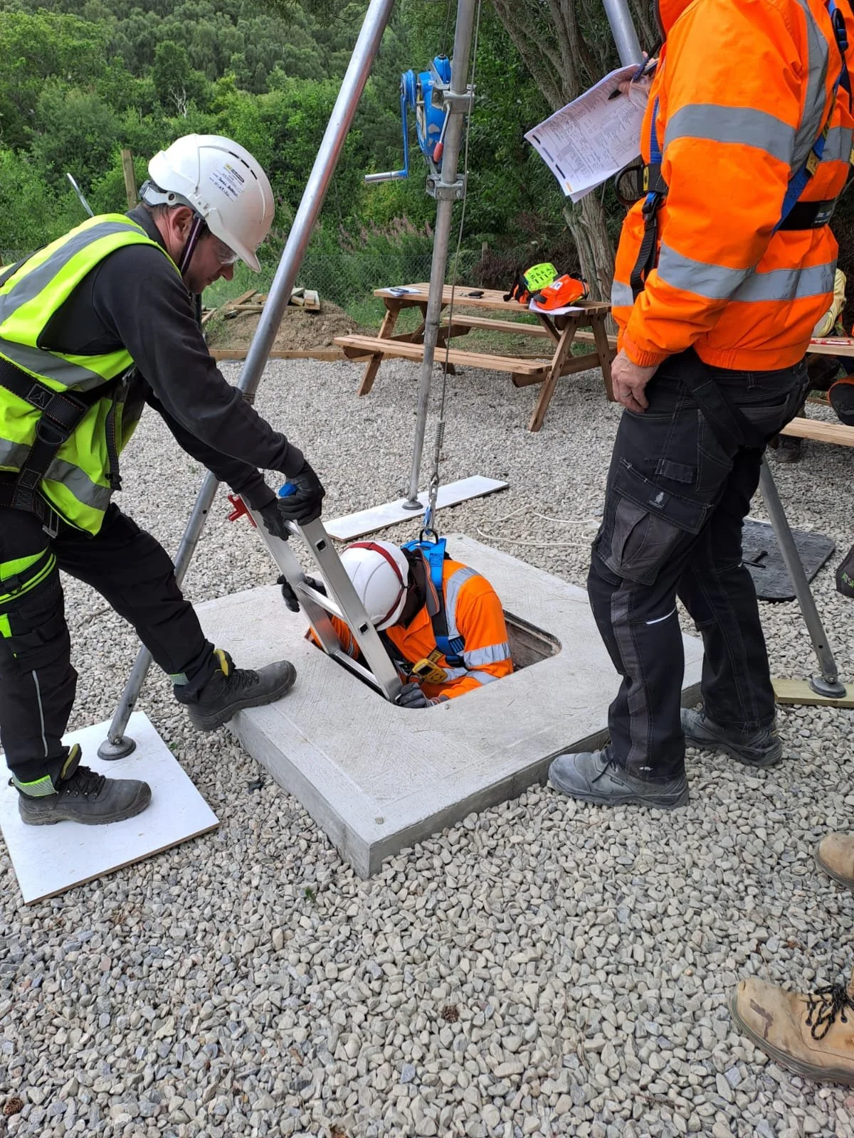 Two workers wearing orange safety uniforms, helmets, and gloves, crouching inside a shipping container, inspecting or working on the interior.
