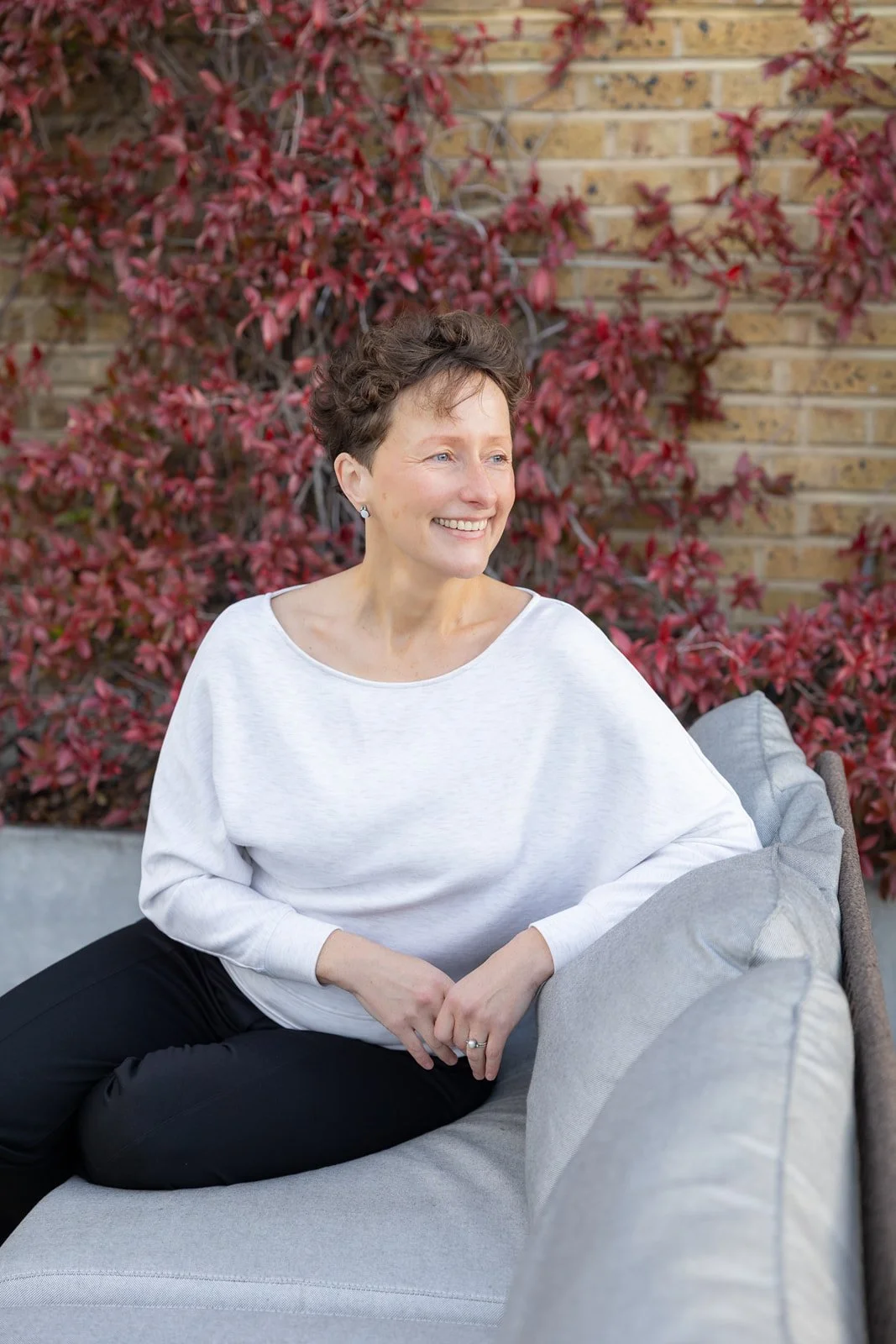 Auste, Crystal Palace osteopath, sitting outdoors against brick wall with autumn foliage