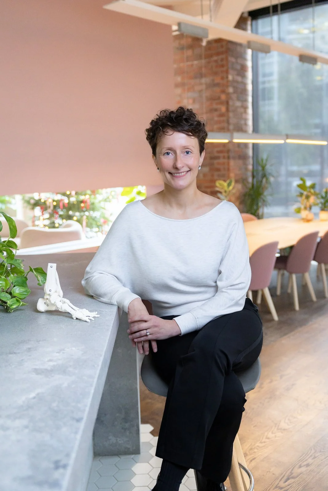 Auste, osteopath and Movement Specialist at Moving Fox Osteopathy, sitting at treatment table in Crystal Palace clinic with exposed brick and natural light