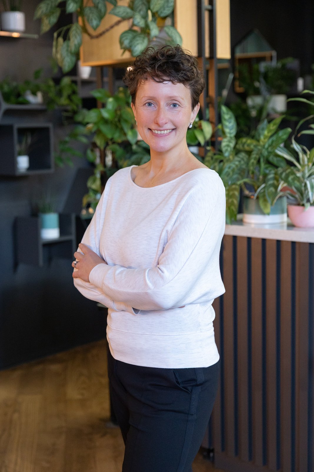 Auste, Crystal Palace osteopath, standing in her clinic with plants and natural light, welcoming new clients