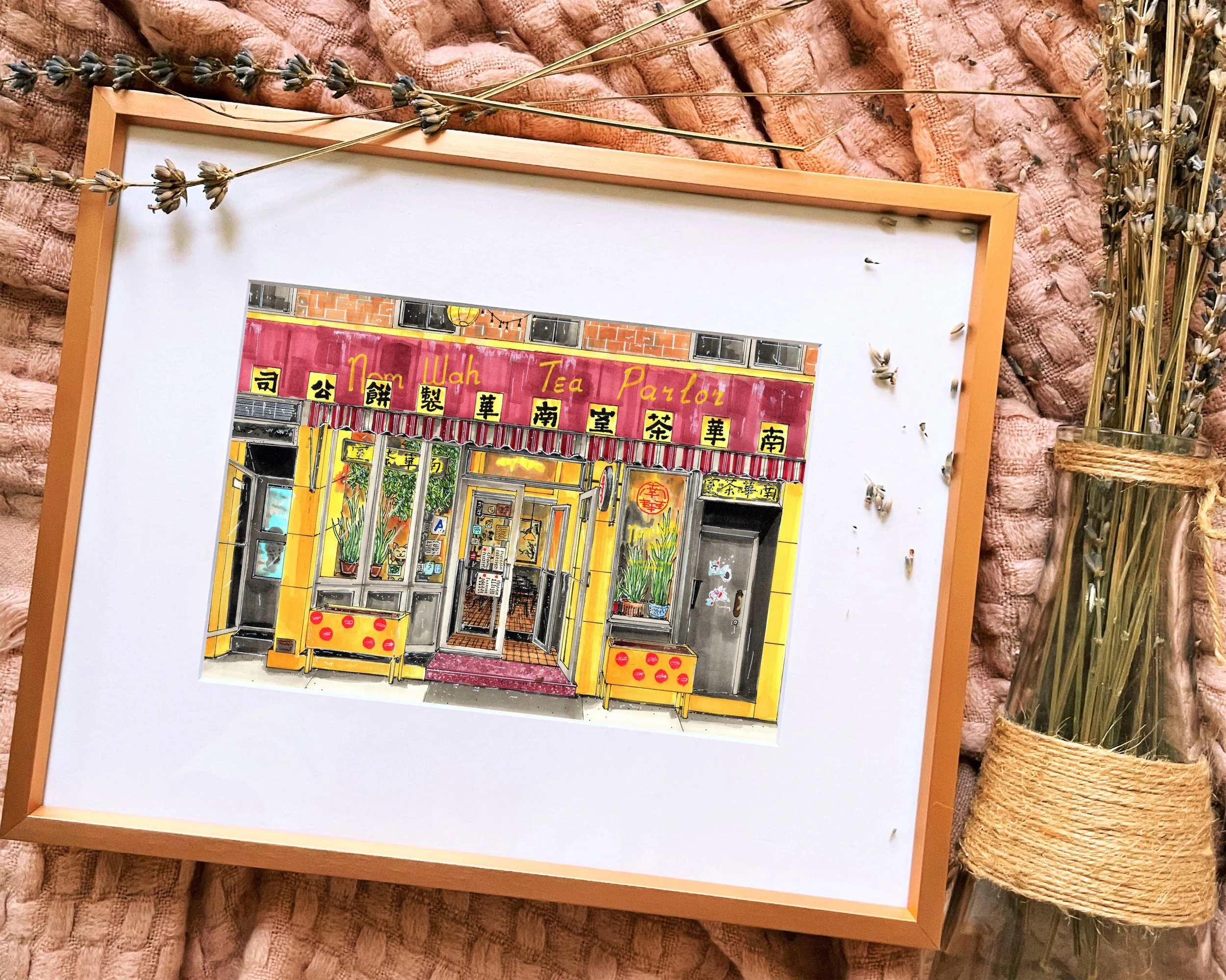 Framed in gold, this hand-illustrated drawing of Nom Wah Tea Parlor print sits on a pink blanket