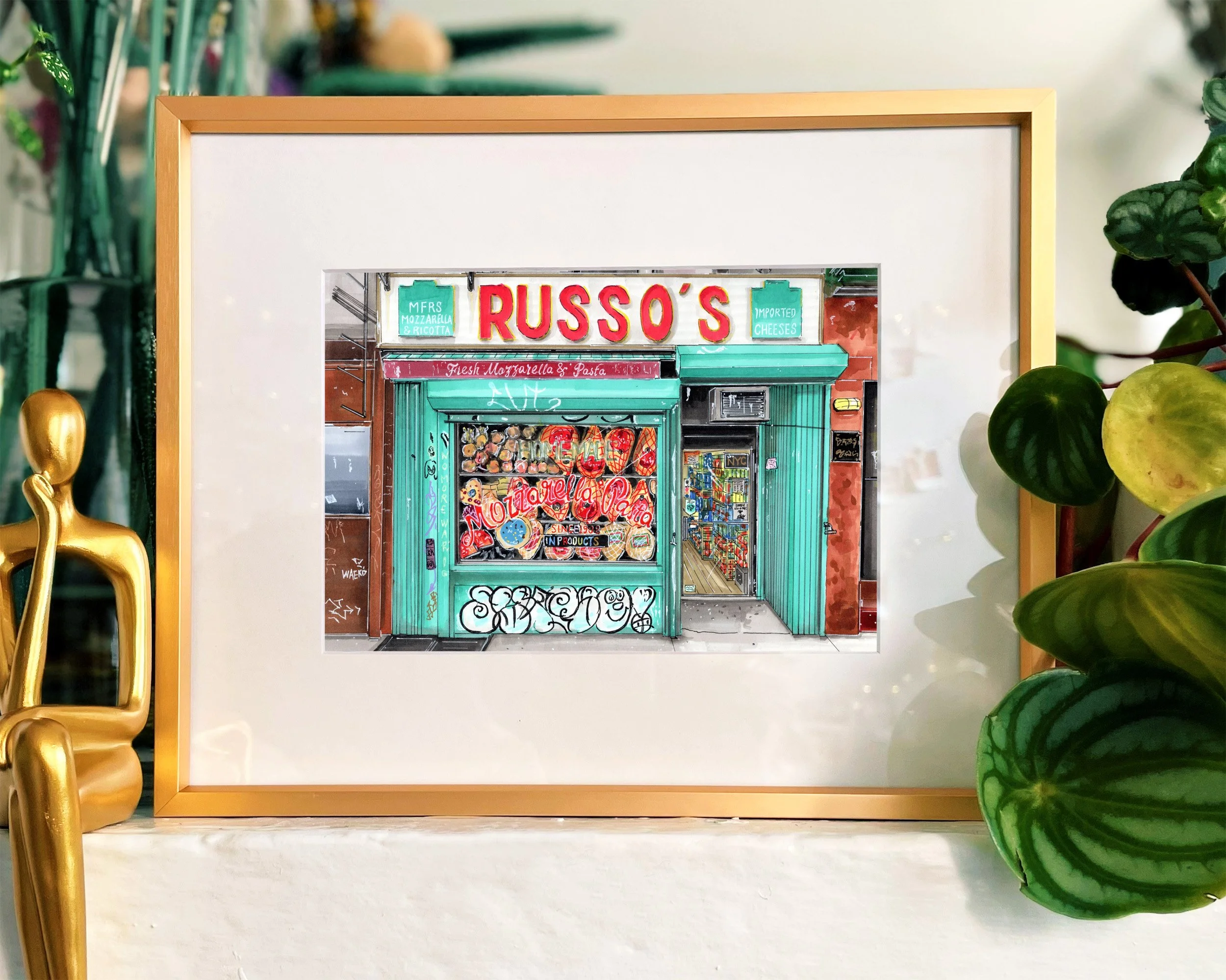 Framed in a gold metal frame, this hand-illustrated drawing of Russo’s Mozzarella and Pasta print hangs on the wall