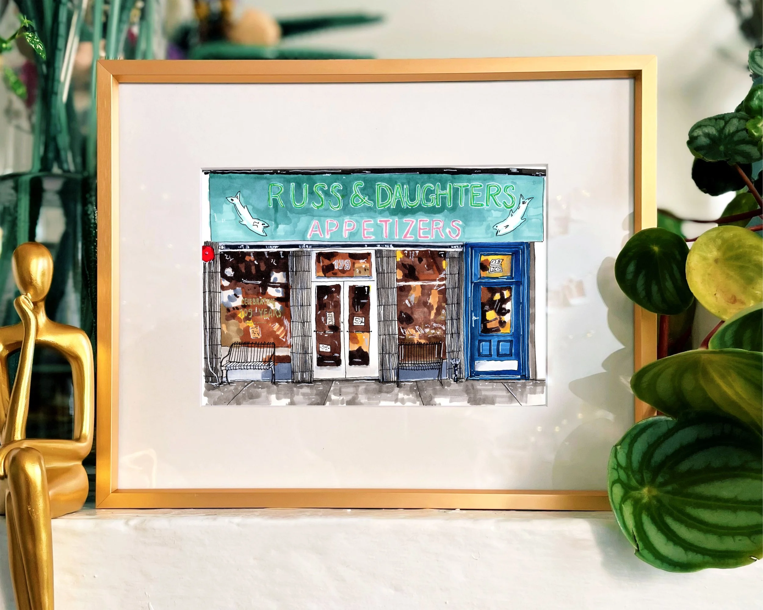 Framed in gold, this hand-illustrated drawing of Russ and Daughters print sits on a mantalpiece