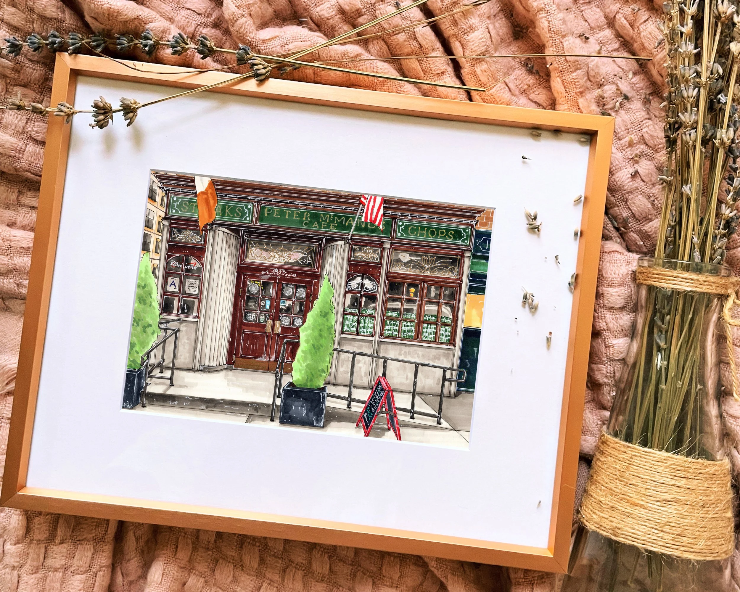Framed in gold, this hand-illustrated drawing of Peter McManus Cafe print sits on a pink blanket