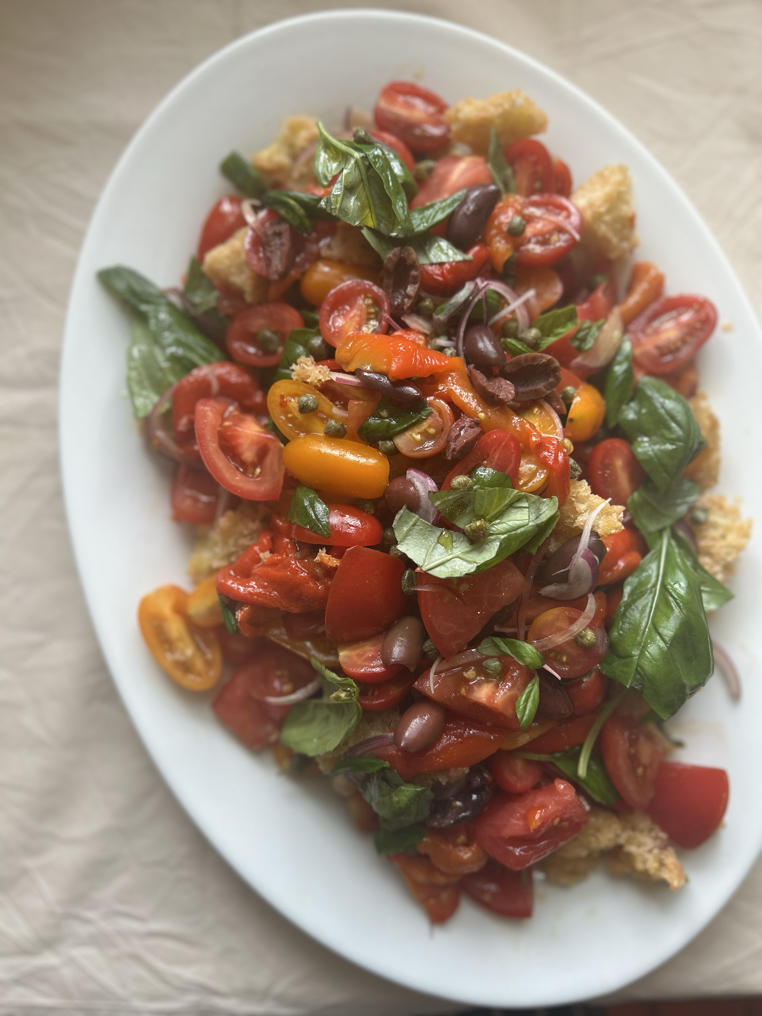 Close-up of a tomato salad with fresh basil leaves on a white oval plate.