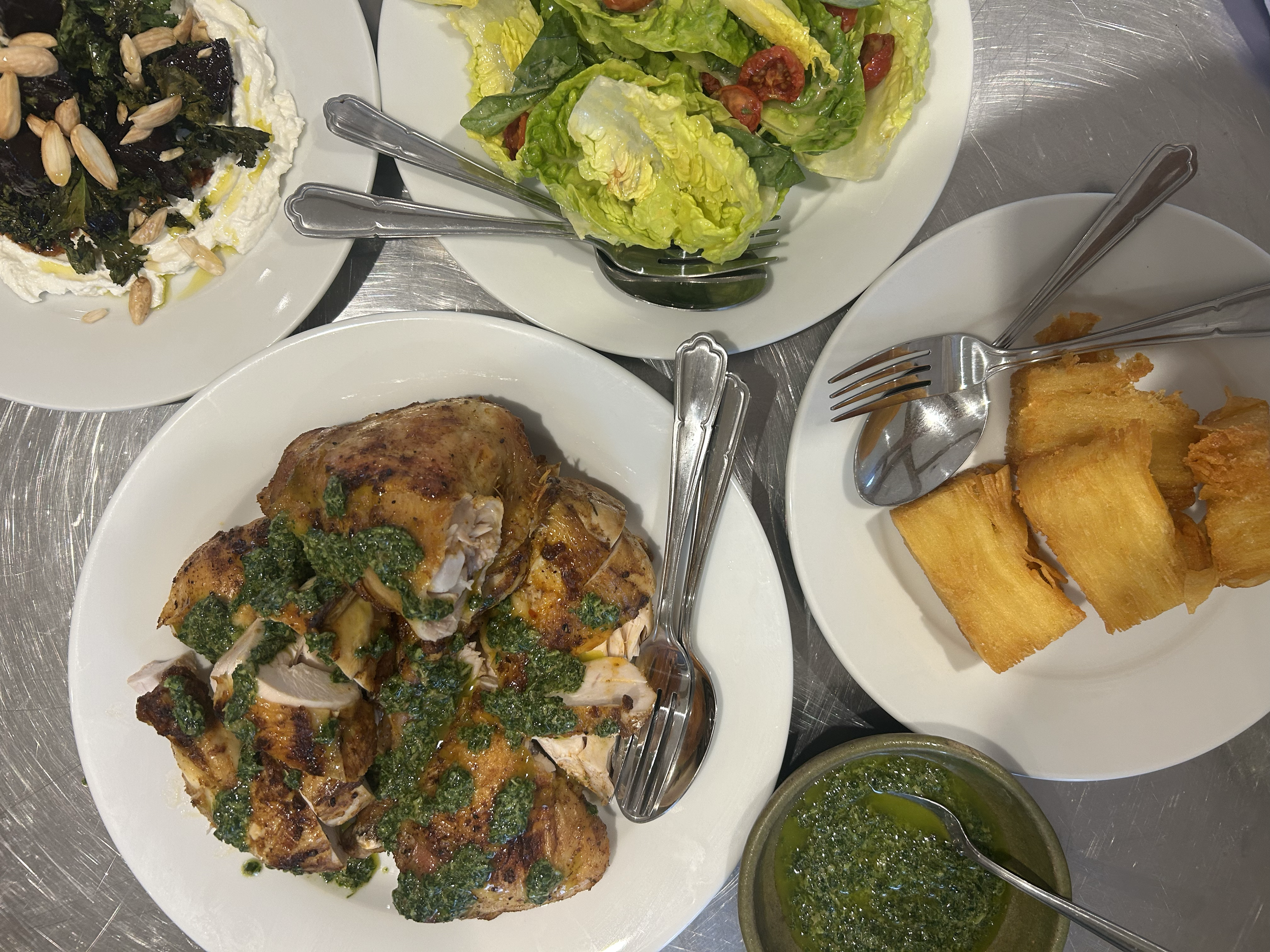 A plate with cooked chicken topped with green herbs and sauce, a small bowl of green sauce, and a side of fresh lettuce salad with cherry tomatoes.