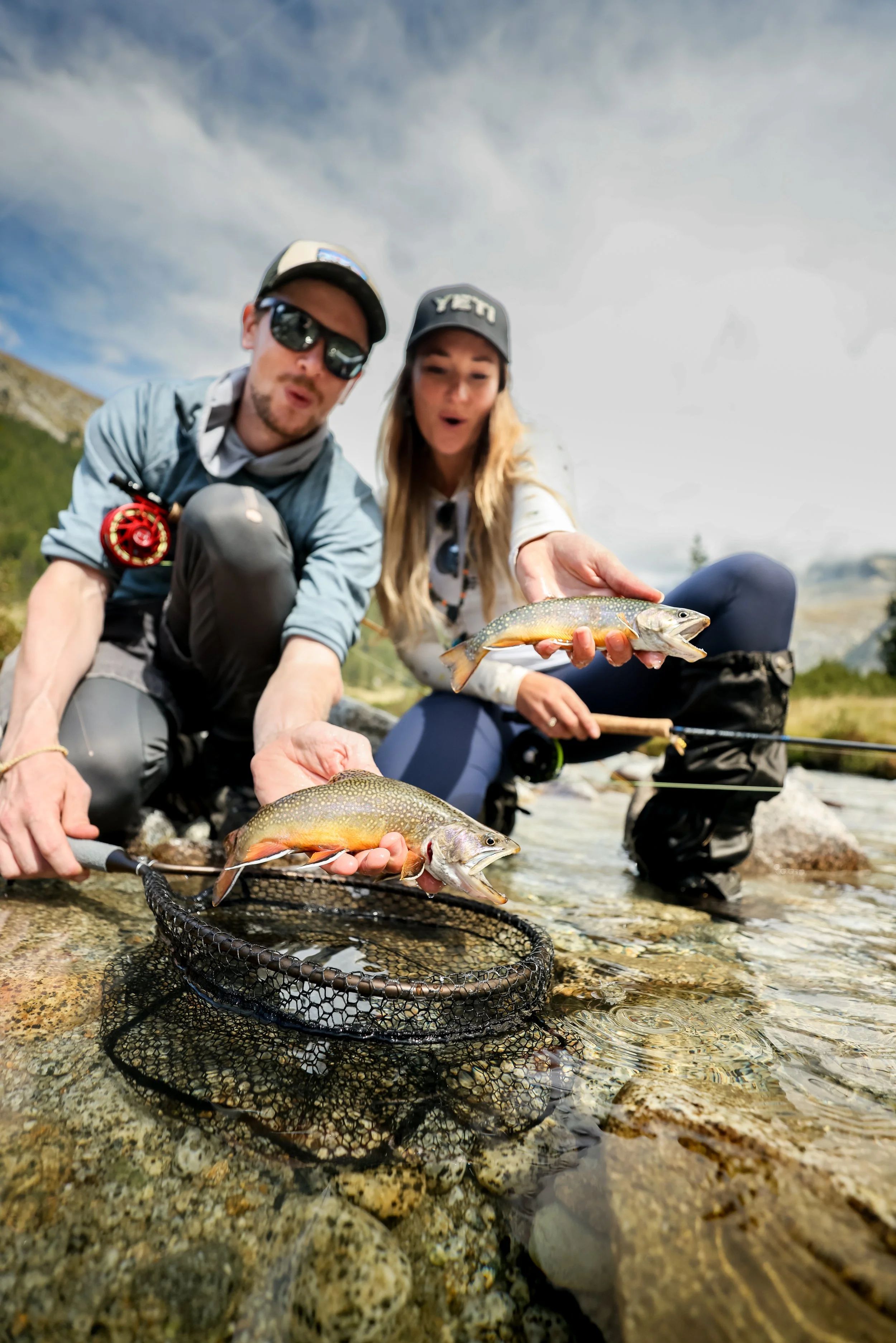 A man and a woman fishing in a stream, holding two brook trout  they caught in the dolomites.
