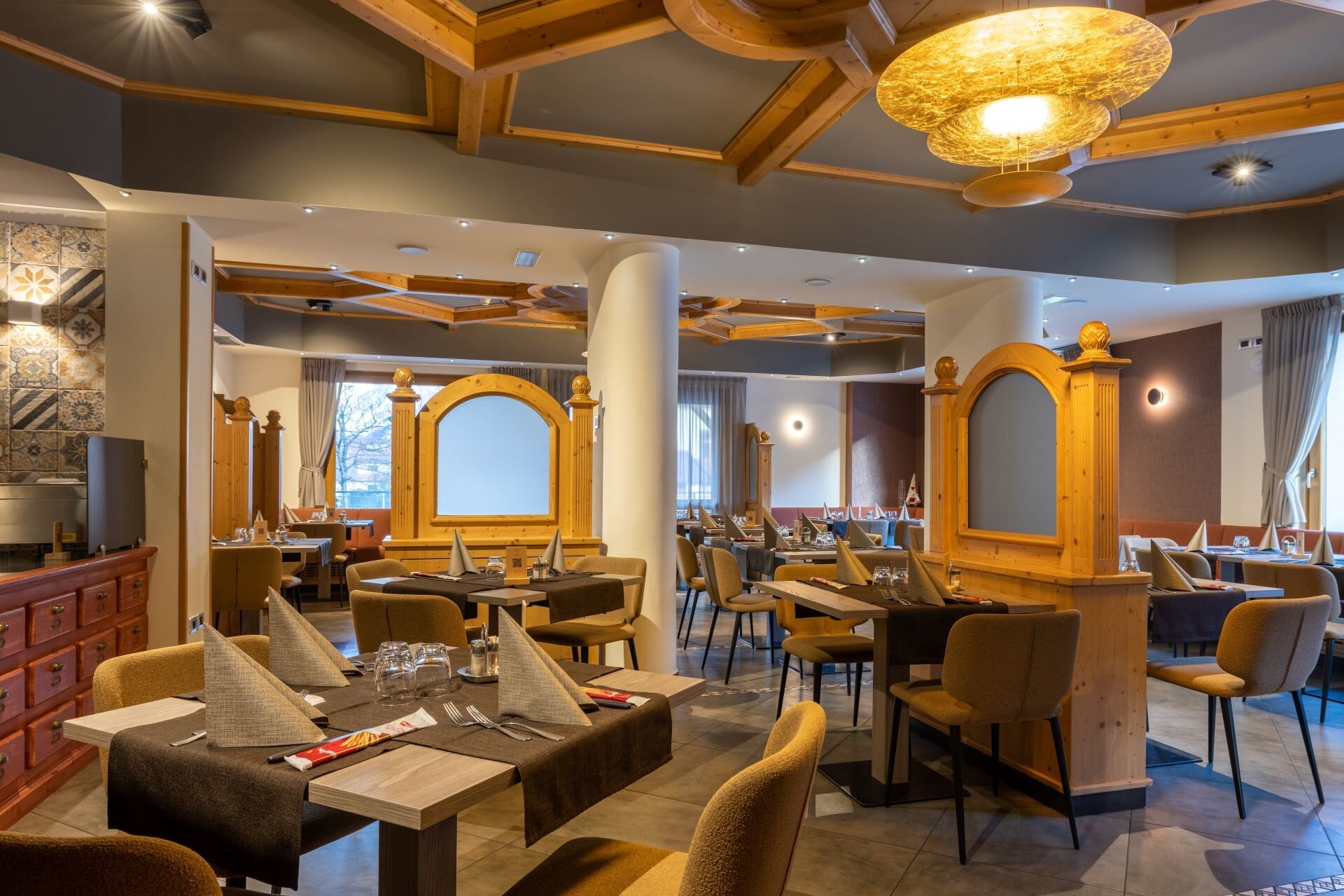 Interior of a restaurant with tables and chairs, wood accents, decorative partitions, and ceiling lighting, ready for guests.