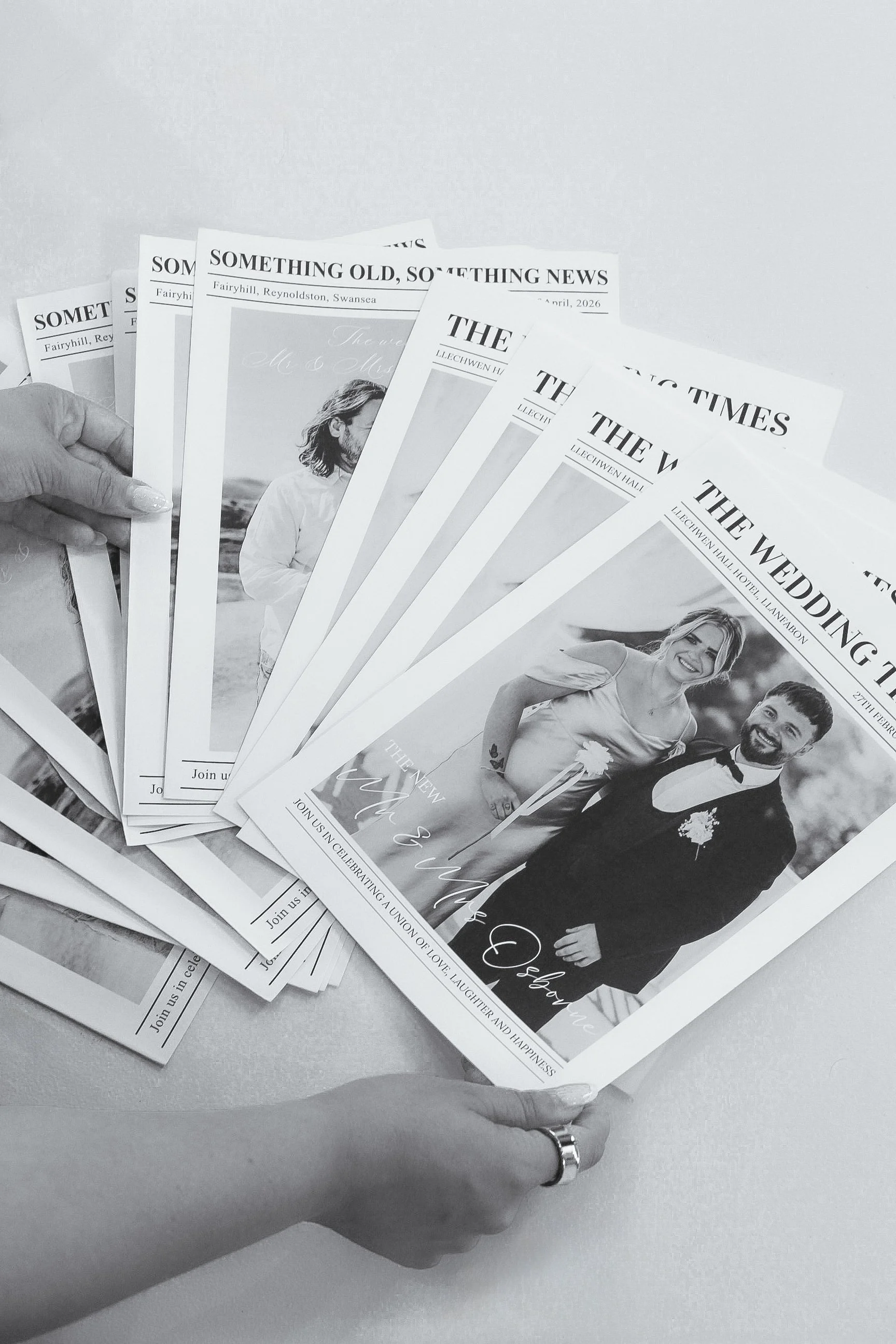 A hand holding several wedding invitation cards featuring a wedding photo of a smiling couple, with text about celebrating their union.