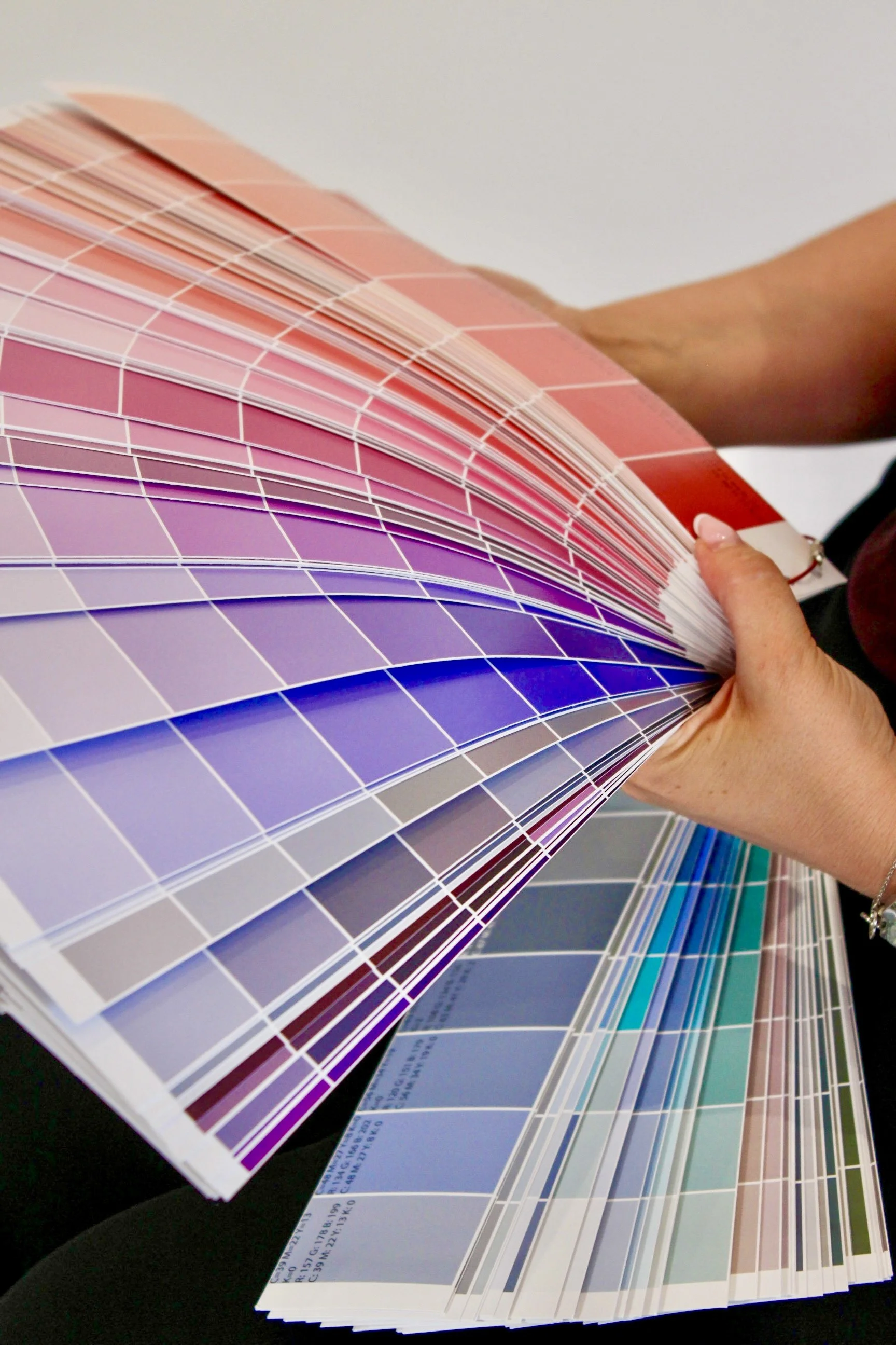 A person holding a large fan deck of various shades of color swatches, fanned out to display multiple color options.