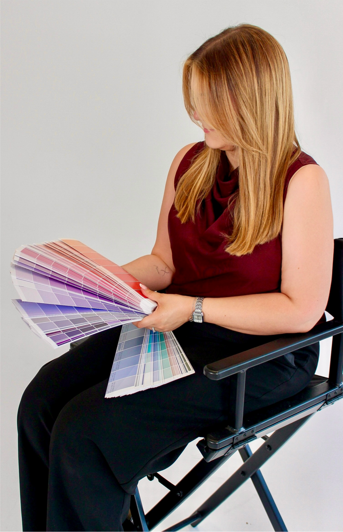 A woman sitting in a chair looking at a color palette sample book with various shades of pink, purple, and blue.