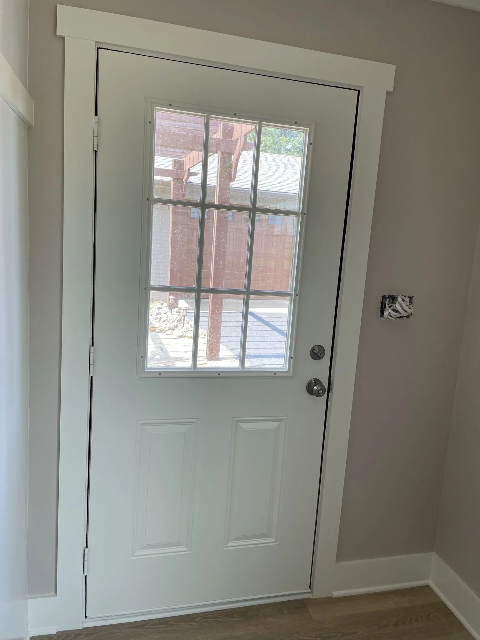 White front door with glass panes, a door handle, and a deadbolt, with a view of a porch and neighboring houses outside.