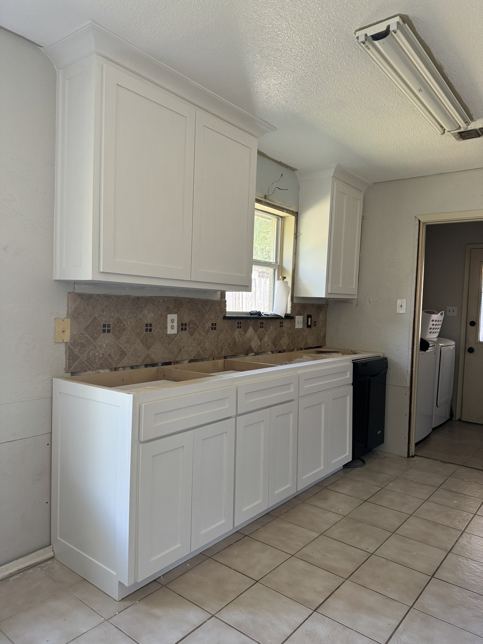 Kitchen with white cabinets, a window, and laundry appliances in a small room to the side.