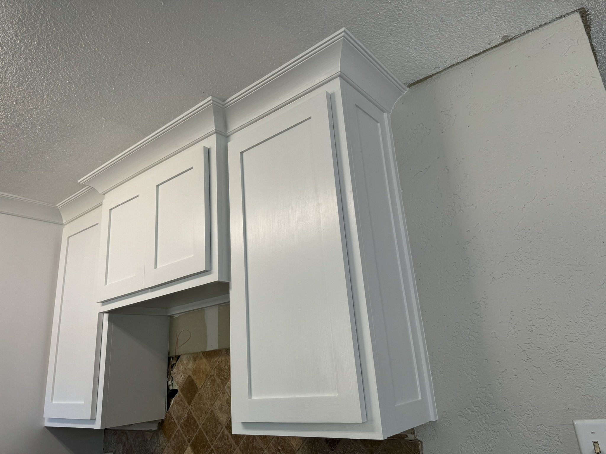 White kitchen cabinets and parts of the kitchen under construction, with exposed wiring and unfinished flooring.