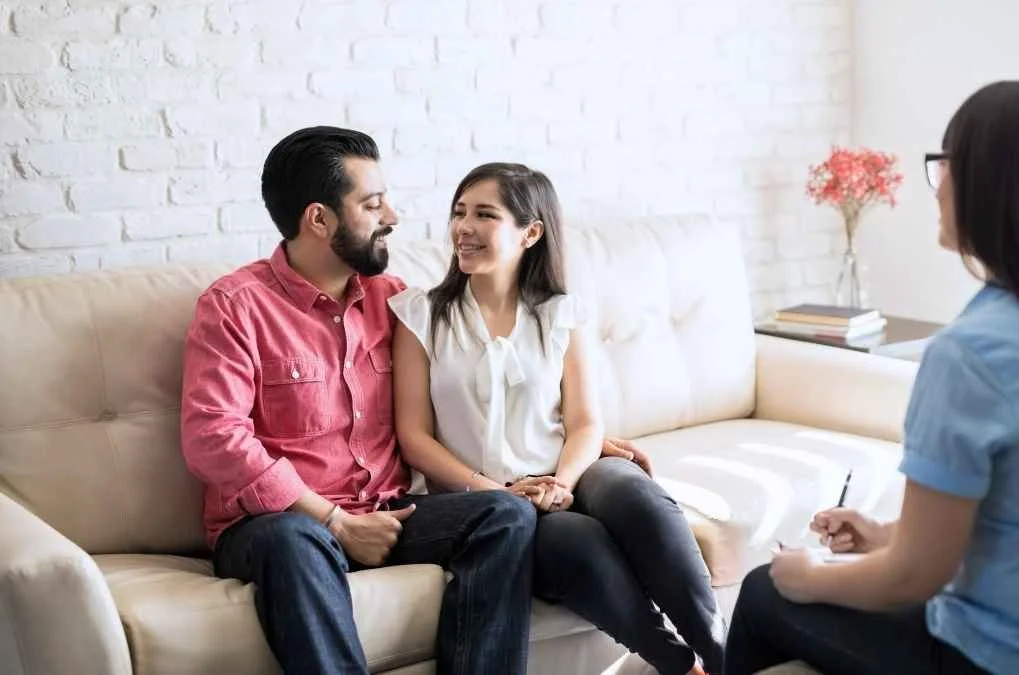 Couple sitting close together on a couch smiling.