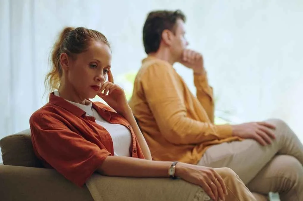 Couple sitting apart on a couch looking distant.