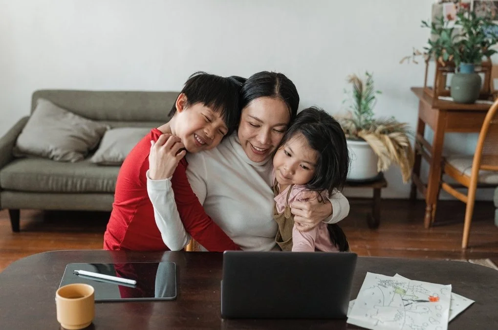 Mother hugging her two smiling children at a table.