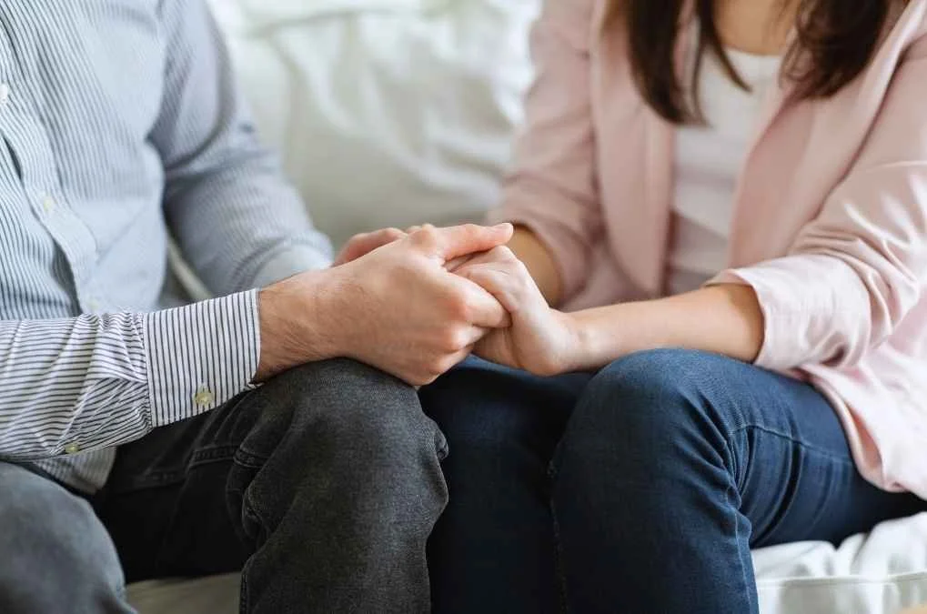 Close-up of a couple holding hands on their laps.