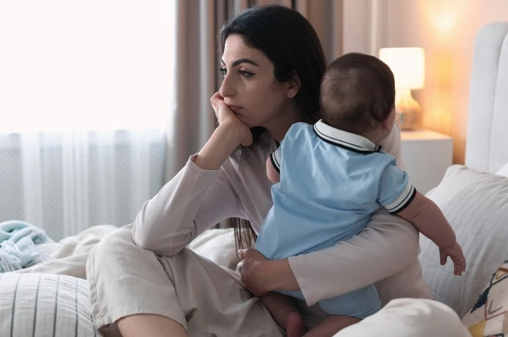 Woman sitting with a baby, looking distracted.
