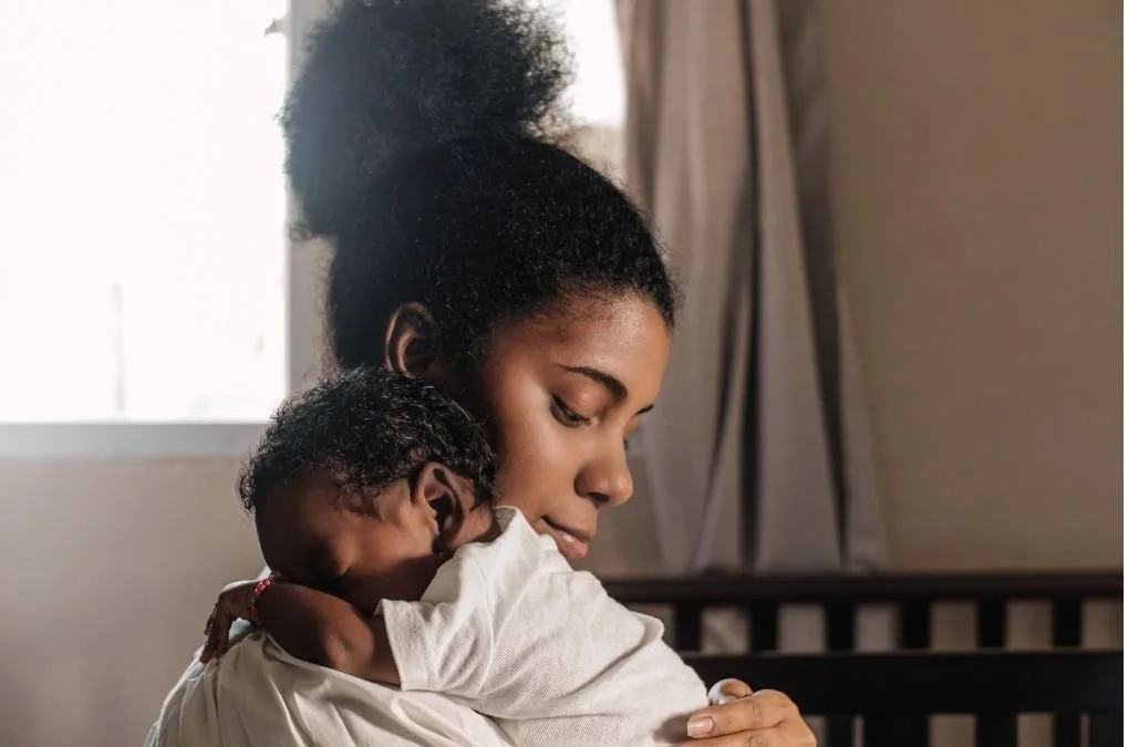 Mother holding her baby close, resting against her shoulder.