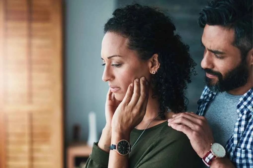 Man comforting a woman with his hand on her shoulder.