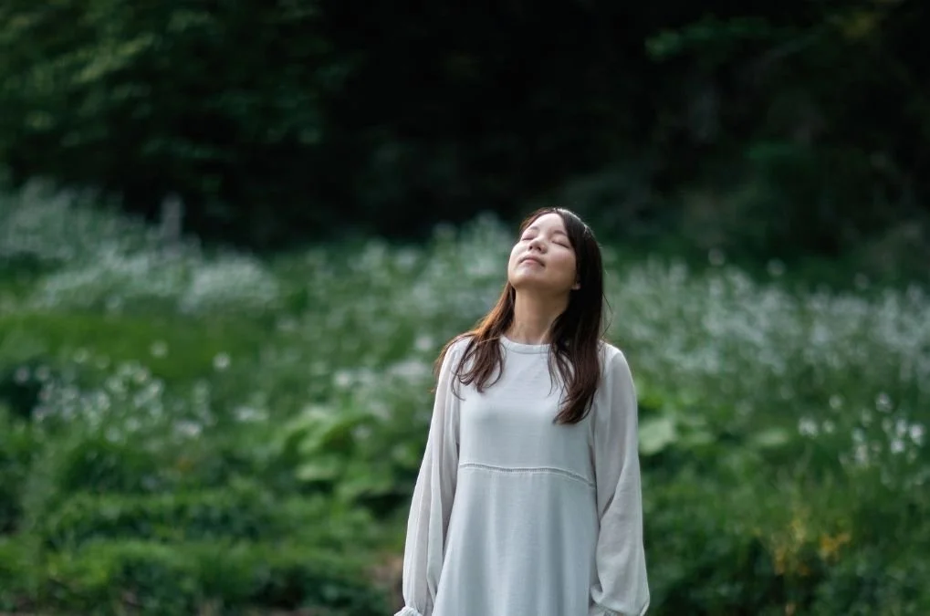 Woman standing in a field with eyes closed, breathing in the air.