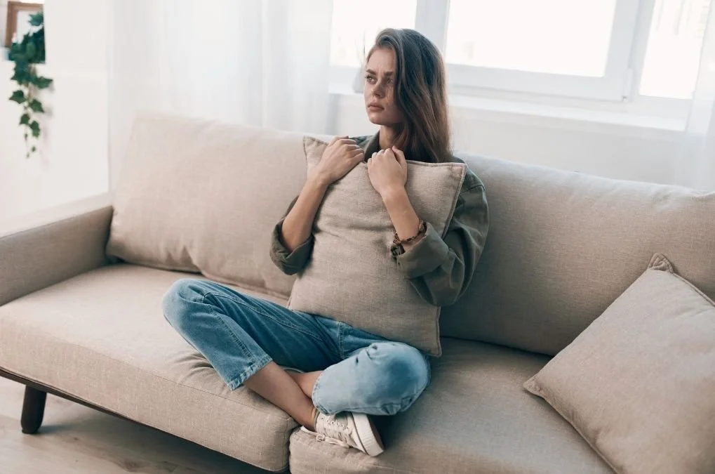 Woman sitting on a couch hugging a pillow, looking away.