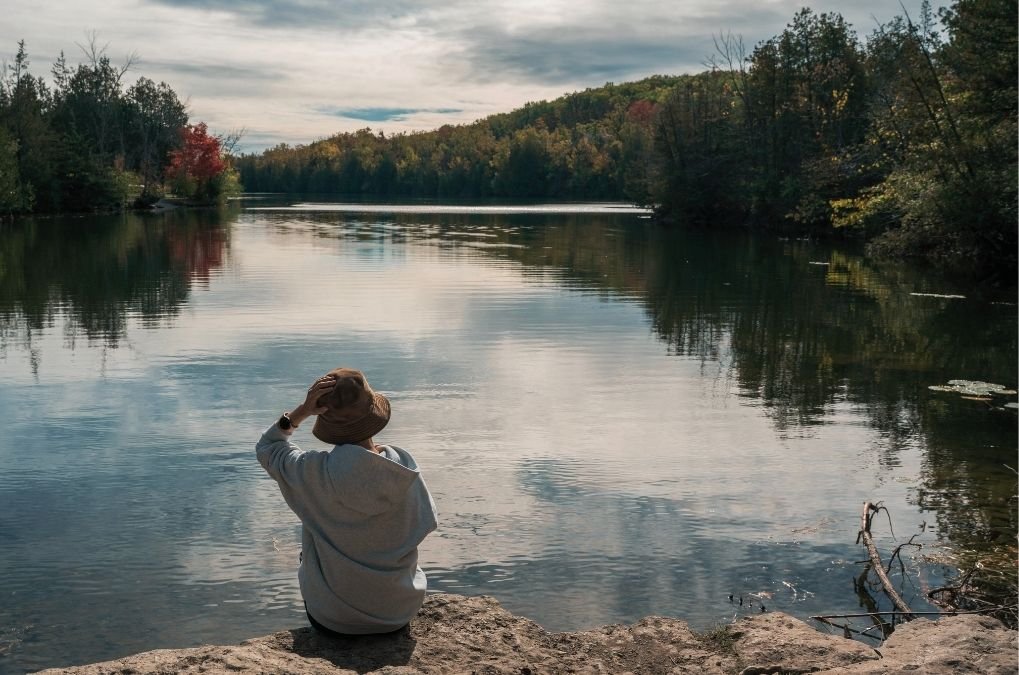 Person sitting by a lake, looking out at the water.