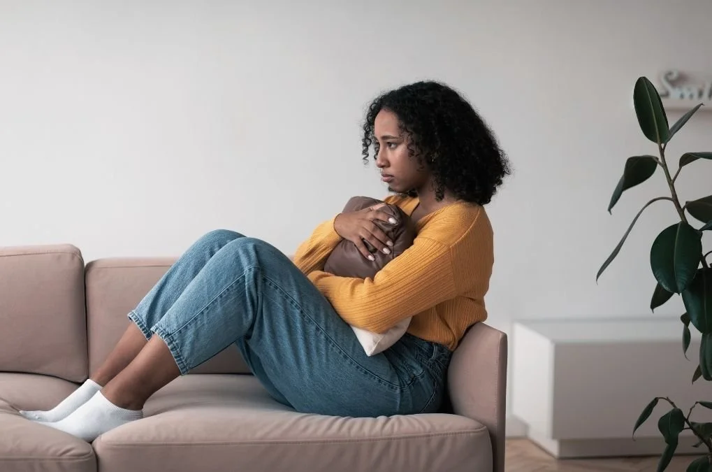Woman sitting on a couch hugging a pillow, looking away.