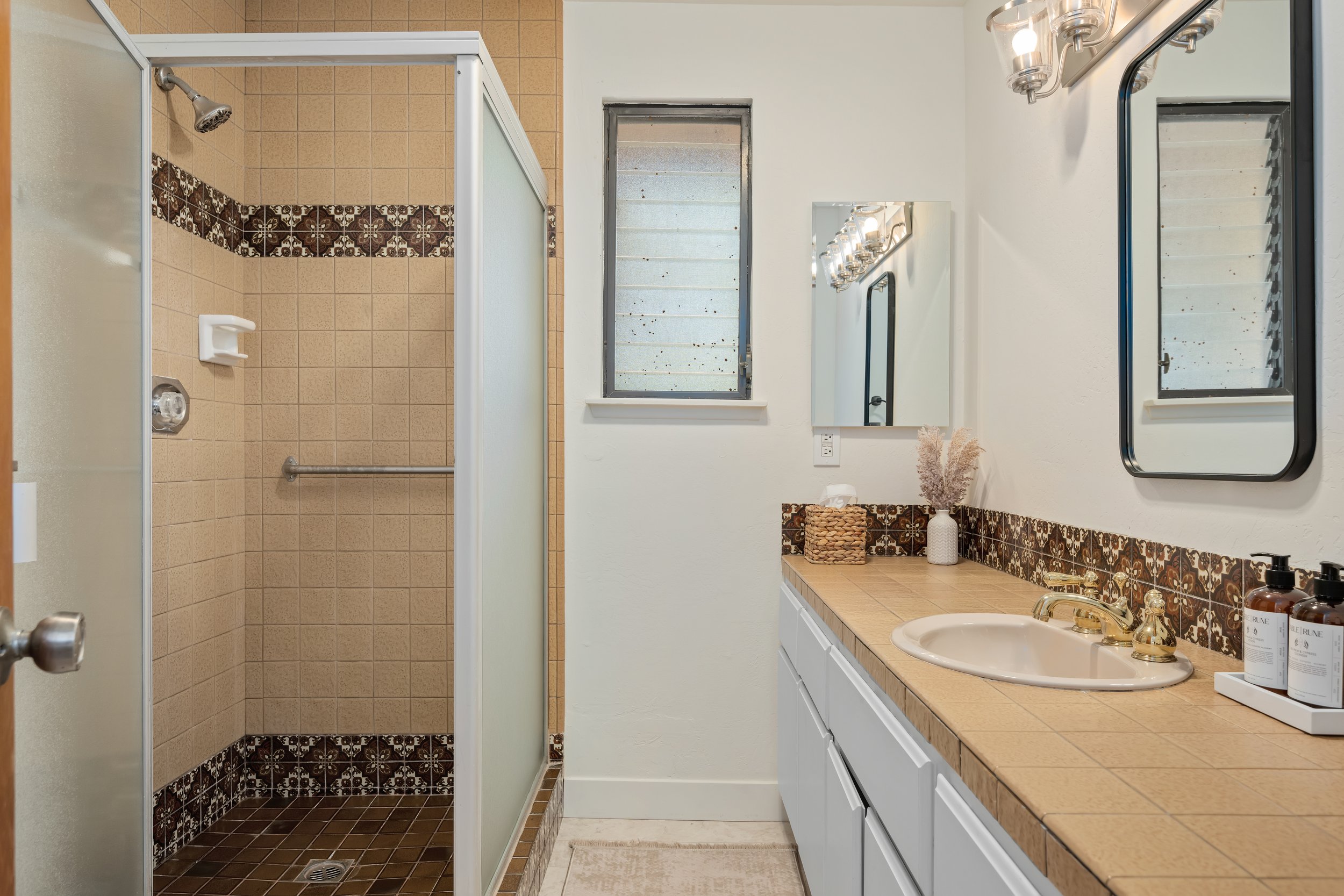 Bathroom with a shower stall, a window above the toilet, a mirror, a vanity with a sink, decorative tiles, and a beige towel on the exercise mat.