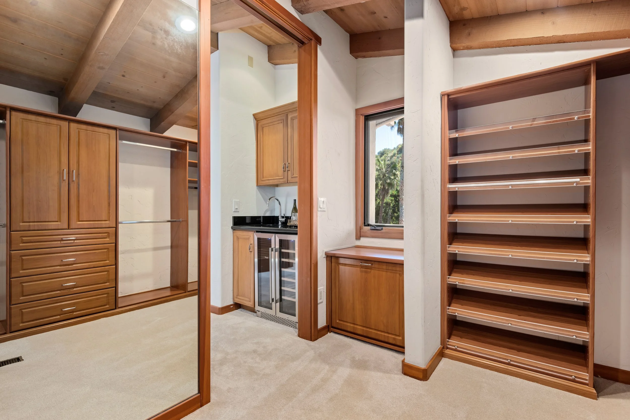 Walk-in closet area with wooden cabinetry, shelves, a small refrigerator, and a window revealing outdoor trees.