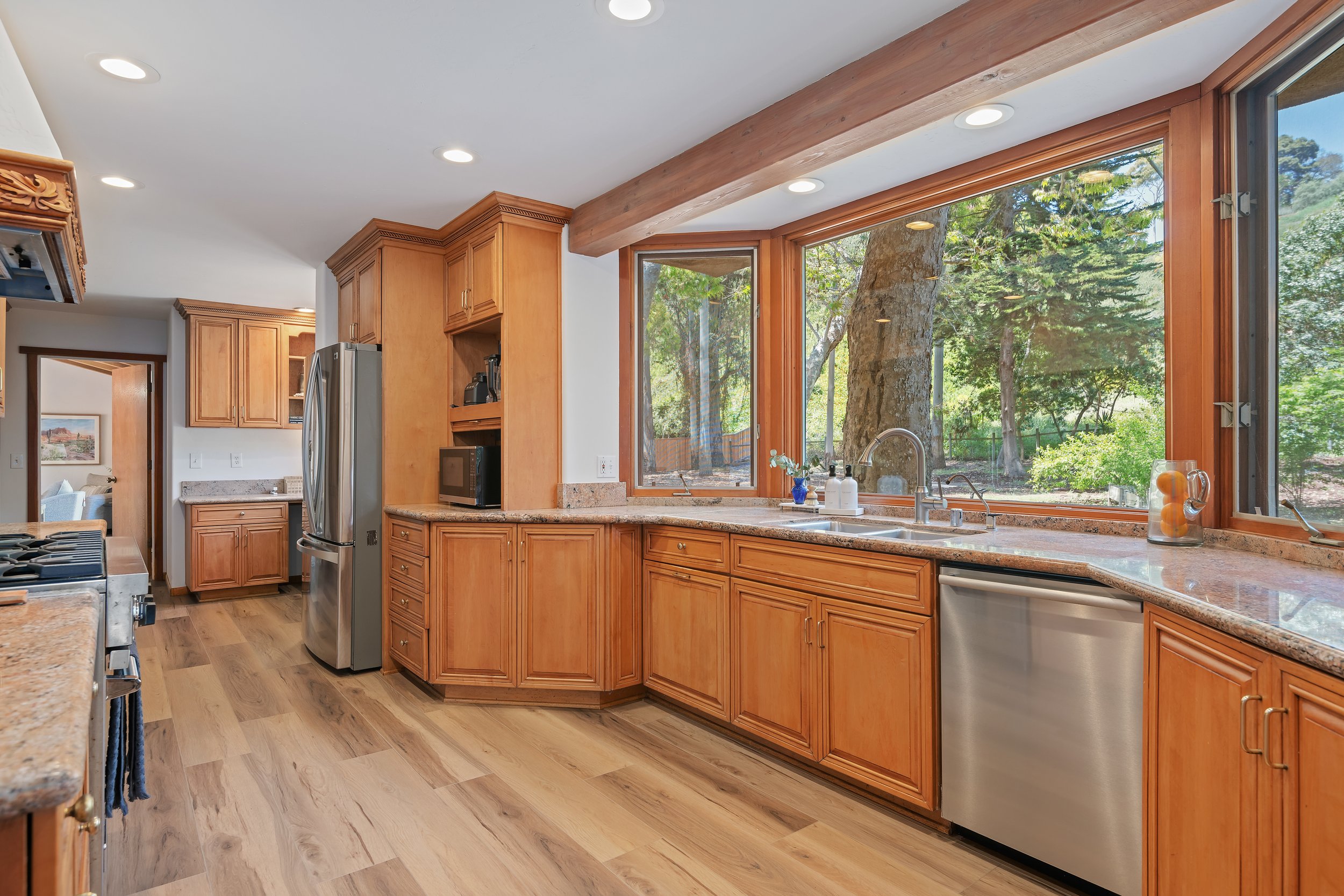 Kitchen with wooden cabinets, granite countertops, stainless steel appliances, and large windows overlooking a wooded yard